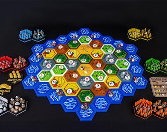 May include: A board game set featuring a central hexagonal grid of terrain tiles with numbered tokens, surrounded by blue water tiles. Includes colored player pieces, resource cards, and a building costs reference card with text.
