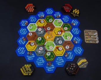 May include: A board game featuring a hexagonal grid of terrain tiles including green forests, yellow fields, brown mountains, and gray hills surrounded by blue water tiles. Includes player pieces, a building costs card, and bonus cards.