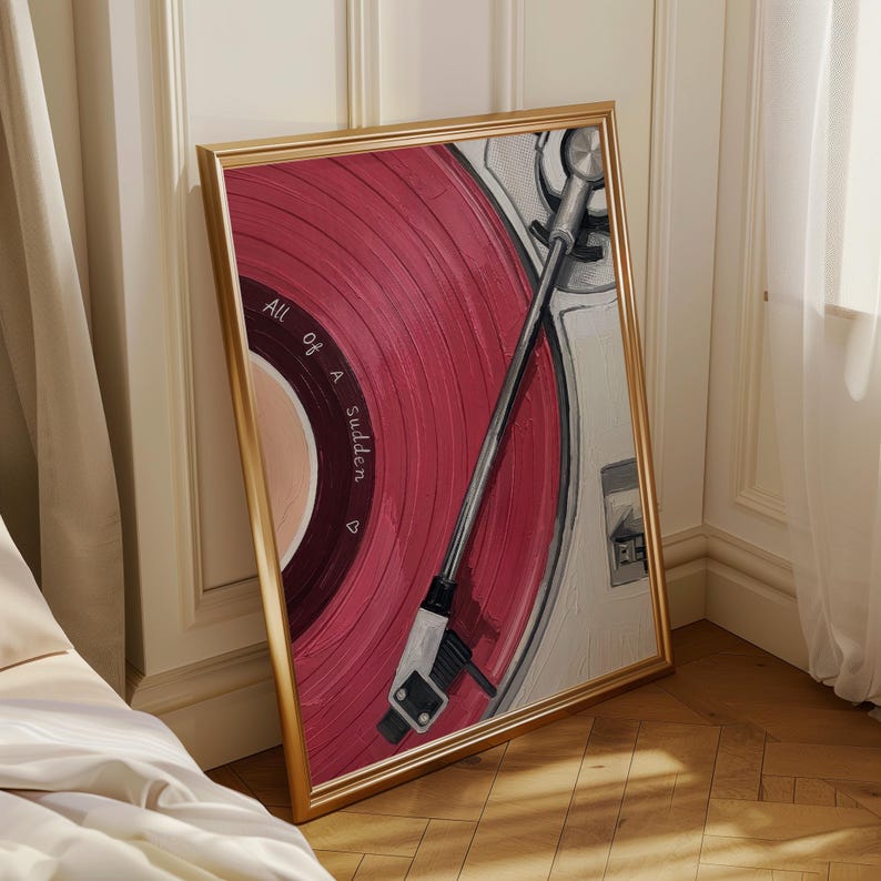 May include: A framed print of a vintage record player with a red vinyl record. The record has the words "All of a Sudden" printed on it. The frame is gold, and the artwork is leaning against a wall.