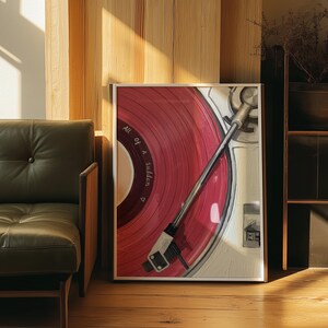 May include: Framed art print featuring a close-up of a red vinyl record on a turntable. The text "All of a Sudden" is visible on the record. The artwork is displayed on a wooden floor, with a green leather chair and wooden wall in the background.