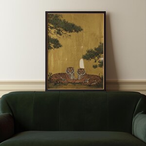 May include: Framed artwork featuring two tigers resting side-by-side. The tigers have orange and black stripes, set against a gold background with green tree branches. The artwork is in a black frame.