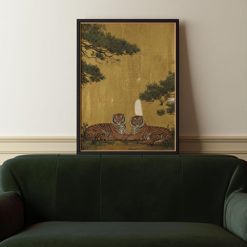 May include: Framed artwork featuring two tigers resting side-by-side. The tigers have orange and black stripes, set against a gold background with green tree branches. The artwork is in a black frame.