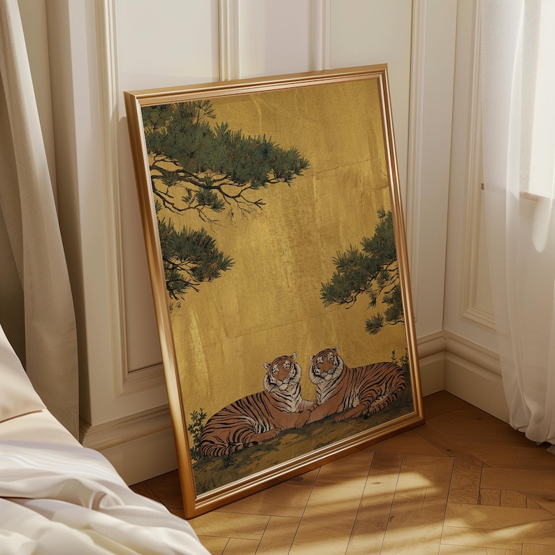 May include: Framed artwork featuring two tigers resting beneath a golden background with green tree branches. The tigers have orange and black stripes. The frame is gold-colored and leans against a wall.