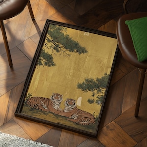 May include: Framed artwork featuring two tigers resting on a hillside, set against a gold background with green foliage. The tigers have orange and black stripes. The frame is dark brown.