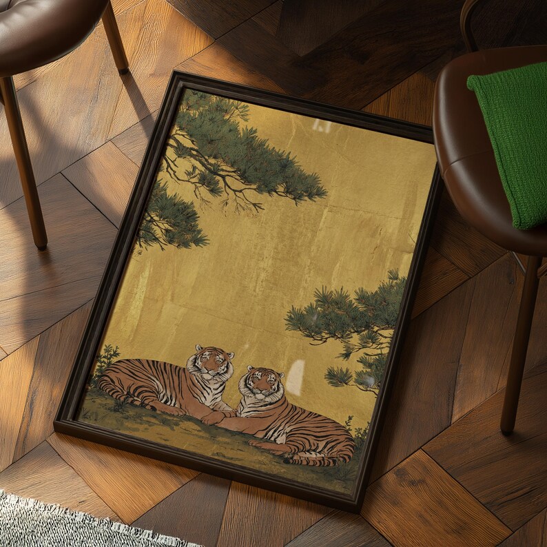 May include: Framed artwork featuring two tigers resting on a hillside, set against a gold background with green foliage. The tigers have orange and black stripes. The frame is dark brown.
