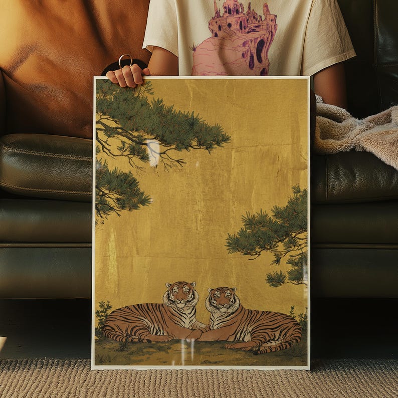 May include: A framed art print featuring two tigers resting side-by-side. The tigers have orange and black stripes, set against a gold background with green tree branches. The artwork is in a white frame.