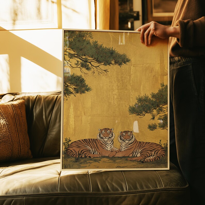 May include: Framed artwork featuring two tigers resting on a bed of grass. The tigers have orange and black stripes, with a gold background and green foliage. The artwork is in a gold frame.