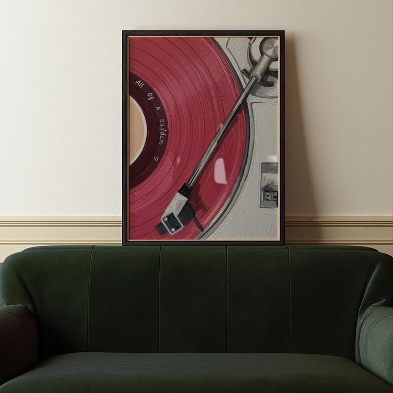 May include: A framed artwork featuring a close-up of a vintage record player with a red vinyl record. The record has the text "All of a Sudden" printed on it. The artwork is in a black frame and is displayed above a green sofa.