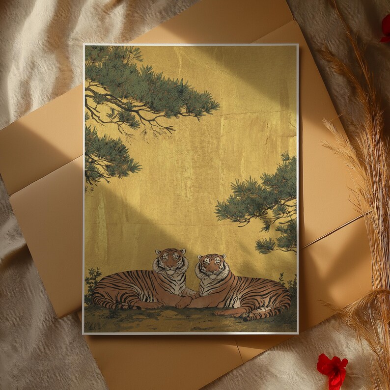 May include: A framed art print featuring two tigers resting side-by-side. The tigers have orange and black stripes, set against a gold background with green foliage. The artwork is displayed on a neutral-toned surface.