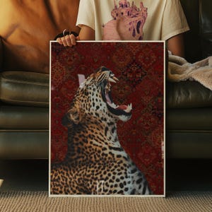 May include: A framed art print featuring a close-up of a leopard yawning, showcasing its teeth and open mouth. The leopard has a spotted coat. The background is a patterned red rug. The print is held by a person.