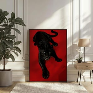 May include: A framed art print featuring a black panther on a red background. The panther is depicted in a realistic style, with detailed fur and piercing blue eyes. The artwork is displayed in a room with a neutral color palette.