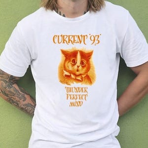 Puede incluir: Camiseta blanca con una ilustración naranja de un gato con pajarita, y el texto "CURRENT '93" encima del gato, y "THUNDER PERFECT MIND" debajo. La camiseta está hecha de un material suave y cómodo.