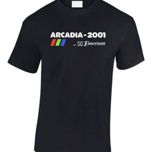 May include: Black t-shirt featuring the text "ARCARDIA-2001" in white, above a red, green, and blue stripe design. Below the text is "by Emerson" in white. The shirt has short sleeves and a crew neck.