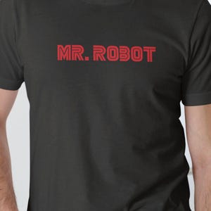 May include: Black t-shirt with the text "MR. ROBOT" in red, block letters. The text is centered on the chest. The shirt is a crew neck style.