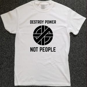 May include: White t-shirt with the text "DESTROY POWER" above a black and white circular graphic, and "NOT PEOPLE" below. The shirt is a crew neck style.
