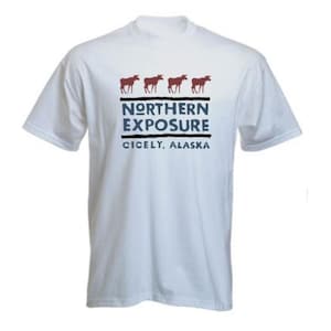 May include: White t-shirt with a crew neck featuring a design with four brown moose above the text "NORTHERN EXPOSURE" and "CICELY, ALASKA" in navy blue. The shirt is made of a soft, comfortable material.