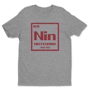 May include: A heather gray t-shirt with a red graphic. The graphic resembles a periodic table element, with "Nin" in large letters, "Nintendium" below, and the numbers "89" and "189.95" above and below.