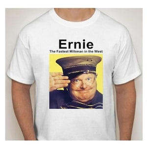 Peut inclure: T-shirt blanc avec un portrait d'un homme portant un chapeau de style militaire et des lunettes, saluant. Le texte "Ernie The Fastest Milkman in the West" est imprimé au-dessus de l'image. Le t-shirt est de style col rond.
