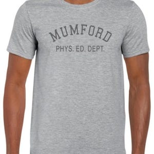 Puede incluir: Una camiseta gris jaspeado de cuello redondo con el texto "MUMFORD" arqueado en la parte superior y "PHYS. ED. DEPT." debajo, en un gris más oscuro. La camiseta de manga corta parece estar hecha de un material suave y cómodo.