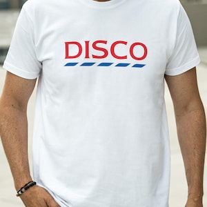 Può includere: T-shirt bianca con la scritta "DISCO" in lettere maiuscole rosse, sopra una serie di linee orizzontali blu. La maglietta è indossata da una persona con la mano in tasca.