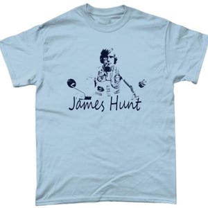 May include: Light blue t-shirt featuring a black and white graphic of a person on a motorcycle, with the text "James Hunt" in a cursive font. The graphic is centered on the front of the shirt.