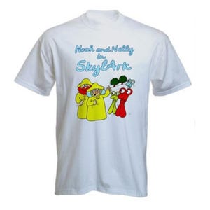 May include: White t-shirt featuring a cartoon graphic with the text "Noah and Nelly in SkyArk." The graphic shows two figures in yellow raincoats and a red and green creature. The shirt is a crew neck style.