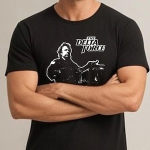 May include: Black t-shirt with a white graphic of a man and the text "THE DELTA FORCE". The graphic is a stylized illustration of a man in a military-style outfit. The t-shirt is made of a soft, comfortable material.