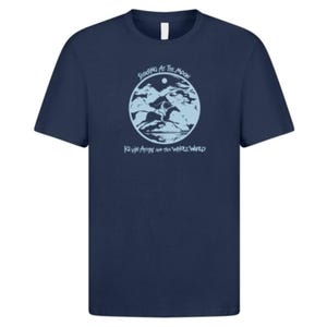 May include: Dark blue t-shirt featuring a light blue circular graphic with a landscape design. The text above reads "SHOOTING AT THE MOON", and below is "KEVIN AYERS AND THE WHOLE WORLD". The shirt has a round neck.