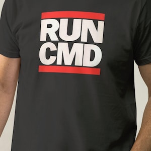May include: Black t-shirt featuring the white text "RUN CMD" within a red rectangular frame. The t-shirt has a crew neck design and is made of a dark fabric.