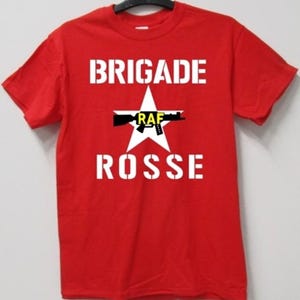 May include: A red t-shirt with the words "BRIGADE ROSSE" in white block letters. A white star with a black rifle graphic and the letters "RAF" in yellow and black is centered on the shirt.