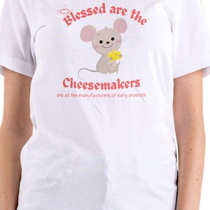 Op de afbeelding: Wit T-shirt met een cartoonmuis die een stuk kaas vasthoudt. De tekst luidt "Blessed are the Cheesemakers" boven de muis, met "and all the manufacturers of dairy products" eronder.