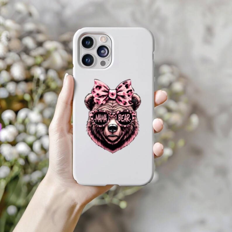 Pu&ograve; includere: Custodia per telefono bianca con un orso rosa e nero che indossa occhiali da sole e un fiocco rosa. Gli occhiali da sole dicono "Mama Bear".