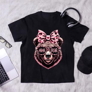 Pu&ograve; includere: Maglietta nera con un orso rosa che indossa occhiali da sole che dicono "Mama Bear" e un fiocco rosa con stampa leopardata.