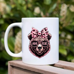 Pu&ograve; includere: Tazza da caff&egrave; in ceramica bianca con un orso rosa e nero che indossa occhiali da sole che recitano "Mama Bear".