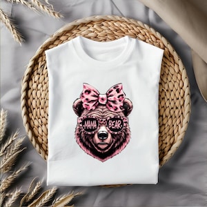 Pu&ograve; includere: Maglietta bianca con un orso rosa che indossa occhiali da sole che dicono "Mama Bear" e un fiocco rosa con stampa leopardata.