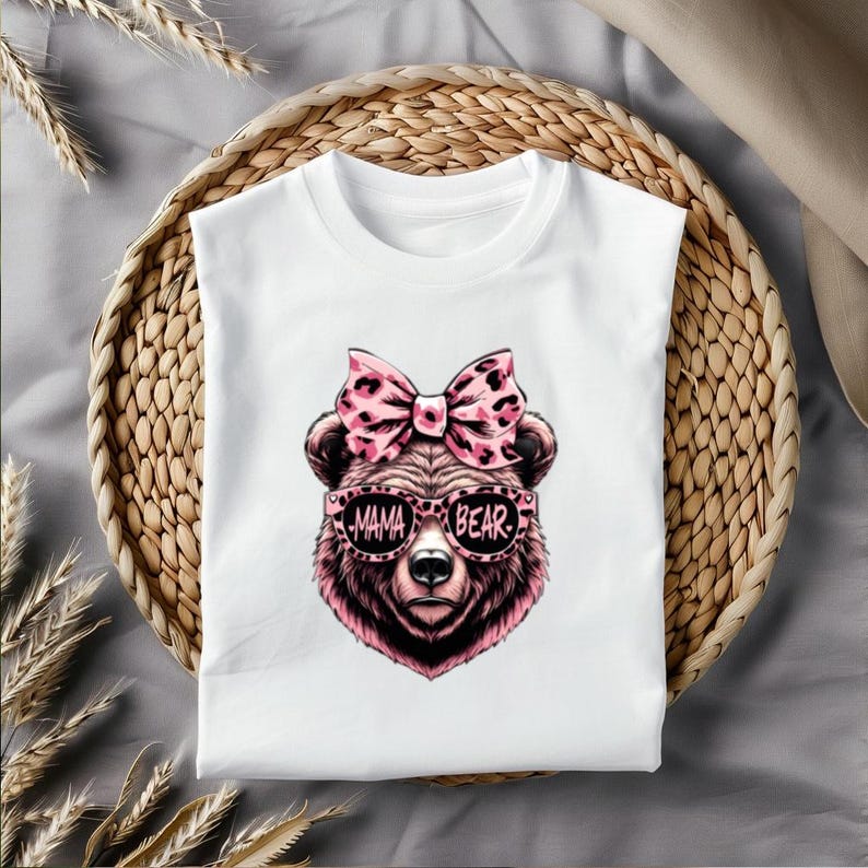 Pu&ograve; includere: Maglietta bianca con un orso rosa che indossa occhiali da sole che dicono "Mama Bear" e un fiocco rosa con stampa leopardata.