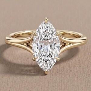 Puede incluir: Un anillo de oro con una gran piedra preciosa transparente de talla marquesa en un engaste de garras. La banda está hecha de oro amarillo pulido y se divide en dos brazos distintos al llegar a la piedra central, creando un diseño abierto.