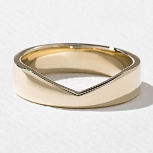Peut inclure: Une bague en or jaune poli présentant une encoche en forme de V ou une découpe en chevron sur le bord supérieur. La surface métallique est lisse et réfléchissante, affichant une construction solide et continue avec un profil épuré et moderne.