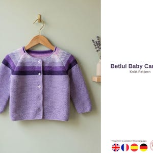 May include: A light purple baby cardigan with a button-up front, hanging on a wooden hanger. The sweater features horizontal stripes of varying shades of purple and the text "Betlul Baby Cardigan Knitt Pattern".