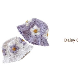 May include: Two crochet daisy caps, one white and one lavender, are displayed against a white background. The caps feature a daisy pattern with white petals and yellow centers. The text "Daisy Cap" is visible.