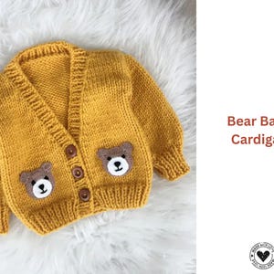 Op de afbeelding: Mosterdgele gebreide babycardigan met berengezichtapplicaties op de voorkant. De cardigan heeft een V-hals, knoopsluiting en geribde manchetten. De tekst "Bear Baby Cardigan" is zichtbaar.