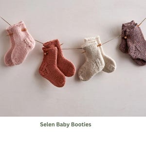 Pode incluir: Uma coleção de botinhas de bebê feitas à mão em tricô, em várias cores, incluindo rosa, ferrugem, bege e roxo, penduradas em uma corda. As botinhas são exibidas em um fundo neutro, mostrando seu design de tricô texturizado.