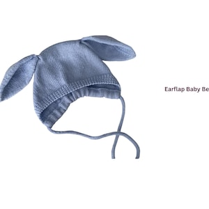 May include: A light blue knitted baby beanie with earflaps and ties. The hat has a bunny ear design and the text "Earfap Baby Beanie". The hat is made of a soft, knitted material.