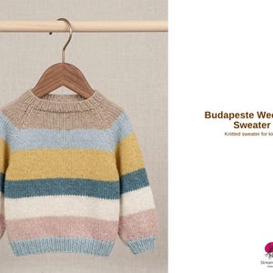 May include: A multi-coloured, striped knitted sweater for children, displayed on a wooden hanger. The sweater has horizontal bands of beige, light blue, yellow, teal, white, and pink. The text "Budapeste Weekend Sweater" is visible.