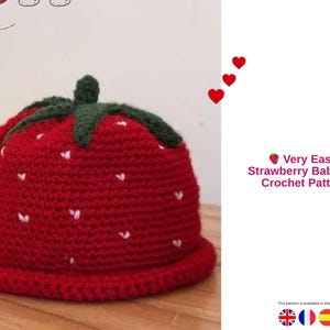 Könnte beinhalten: Ein roter Häkelhut für Babys in Erdbeerform mit grünem Stiel und weißen Samen. Der Hut hat einen Rand und den Text "Very Easy Strawberry Baby Hat Crochet Pattern".