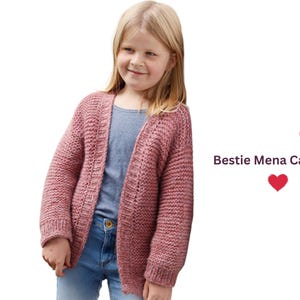 May include: A girl wearing a dusty rose-coloured, open-front cardigan. The chunky knit sweater is paired with a blue top and jeans. The text "Bestie Mena Cardigan" is displayed in the image.