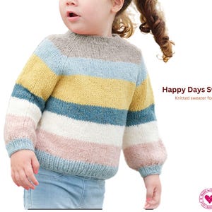 May include: A knitted children's sweater with horizontal stripes in shades of grey, pale blue, yellow, teal, pink, and white. The text "Happy Days Sweater" is visible. The sweater has a round neck and long sleeves.