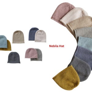 May include: A collection of knitted beanies in various colors, including blue, gray, pink, and mustard yellow. The text "Nebila Hat" is displayed in red. The hats are arranged in a semi-circular pattern, showcasing the range of available colors.
