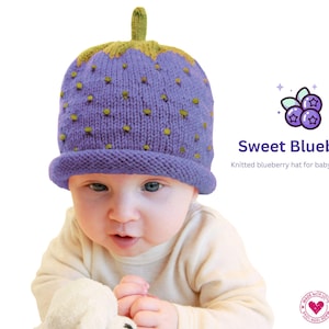 Könnte beinhalten: Eine gestrickte Blaubeermütze für Babys und Kinder. Die Mütze ist lila mit kleinen gelben Punkten und einem grünen Stiel. Der Text "Sweet Blueberry" wird neben einer Blaubeer-Grafik angezeigt.