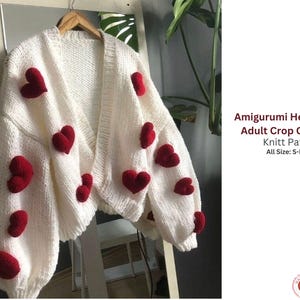 Op de afbeelding: Een crèmekleurig vest met open voorkant, versierd met rode hartmotieven. De cropped trui heeft een V-hals en lange mouwen. De tekst op de afbeelding luidt "Amigurumi Heart Motif Adult Crop Cardigan Knitt Pattern All Size: S-M-L-XL."